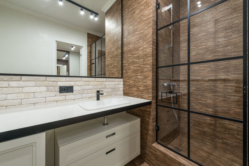 Reforma de baño realizada por Hola Reformas: madera, ladrillo blanco y mampara de acero
