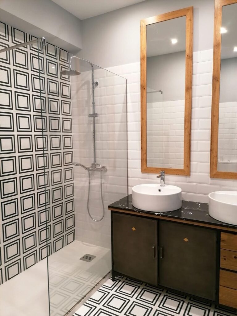 Baño reformado con doble lavabo, azulejo geométrico y ducha a ras de suelo